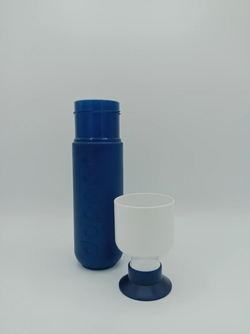 Nachhaltige Trinkflasche Dopper Original Pacific Blue aus biobasierten Materialien mit ikonischem Design in Blau, stehend mit geöffnetem Becherdeckel.