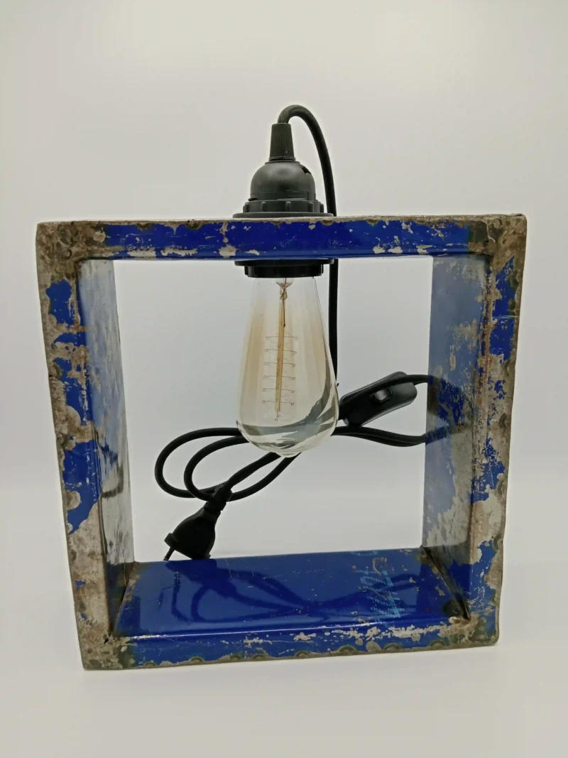Handgefertigte Lampe aus recycelten Ölfässern mit schwarzem Textilkabel und warmweißer Vintage-Glühbirne. Nachhaltiges Design aus Burkina Faso.