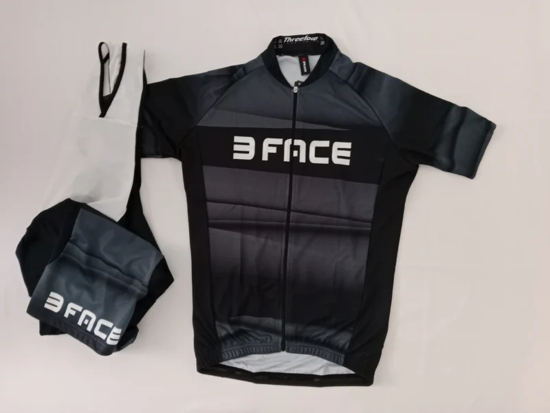 Schwarzes Spicy Radsporttrikot mit kurzem Arm, drei Rückentaschen und elastischem Bund, auf weißem Hintergrund fotografiert.