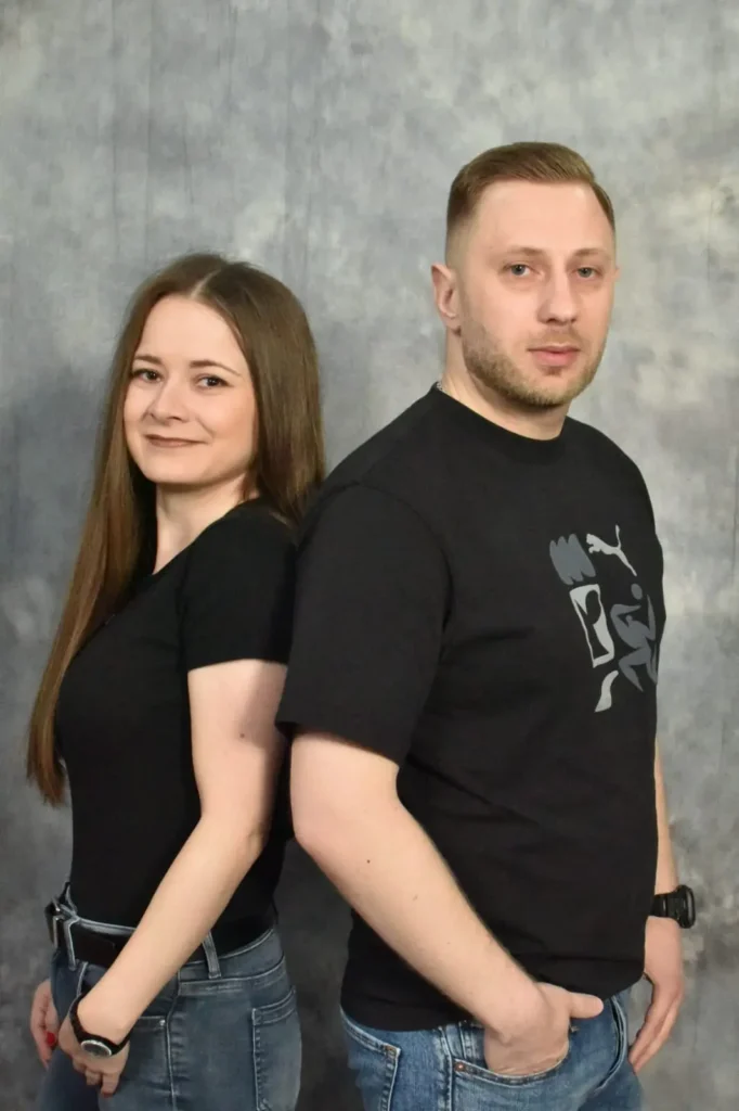 Porträtfoto von Amel und Anela in schwarzer Kleidung vor grauem Studiohintergrund, beide stehen seitlich nebeneinander und blicken in die Kamera.